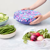 Person holding a floral-patterned reusable bowl cover over a bowl on a light surface.