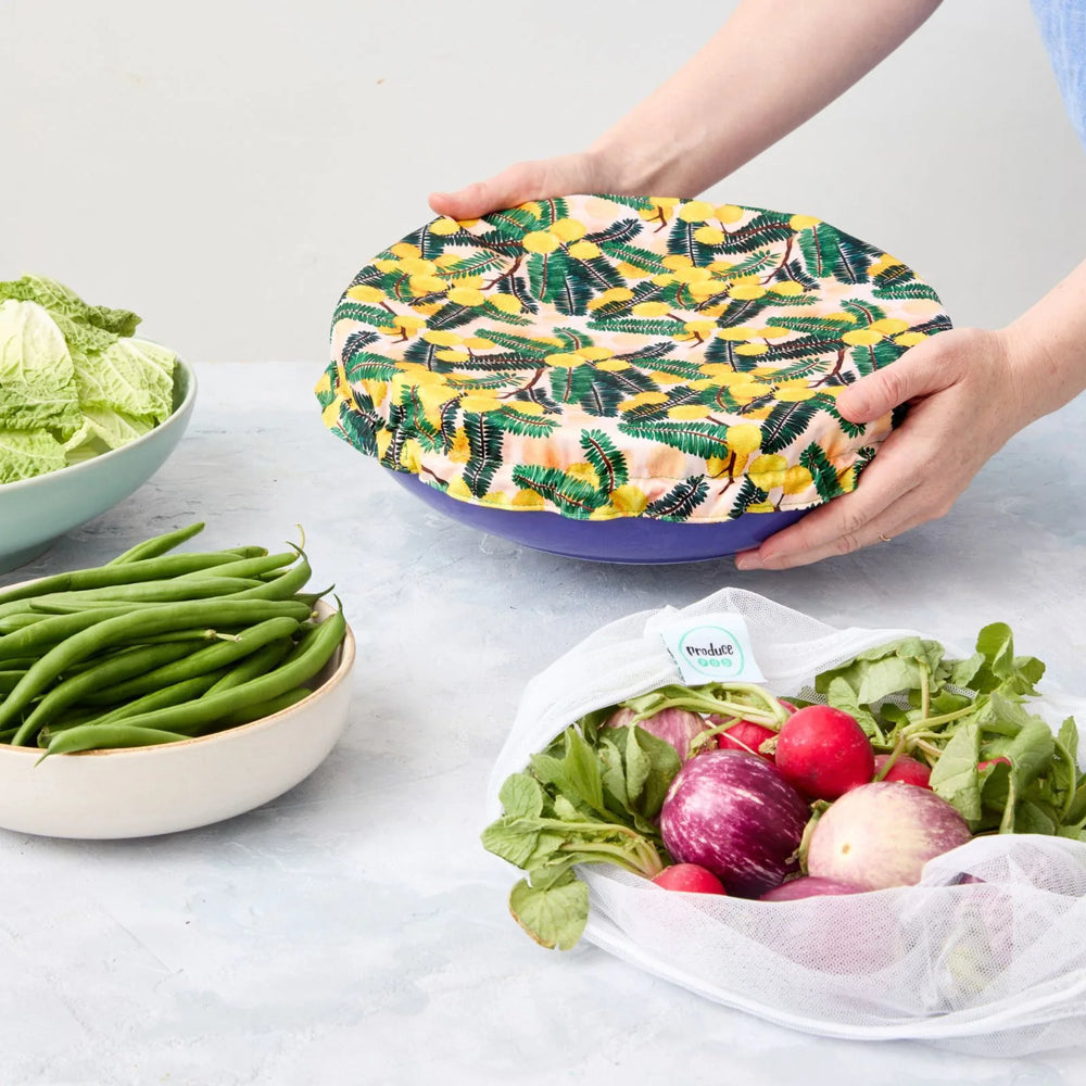 Person holding a floral-patterned reusable bowl cover over a bowl on a light surface.