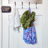 Green leafy vegetables in a reusable shopper bag hanging on a white door with hooks.