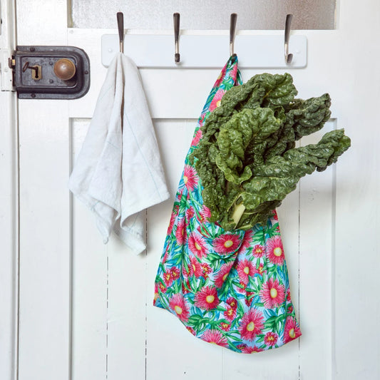 Green leafy vegetables in a reusable shopper bag hanging on a white door with hooks.