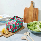 Pink floral reusable produce bag on a kitchen counter with a bowl of lettuce, cutting board, and lemons.