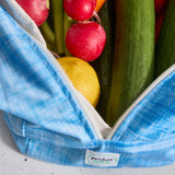Blue reusable produce bag filled with fresh produce including radishes, a lemon, and cucumbers.