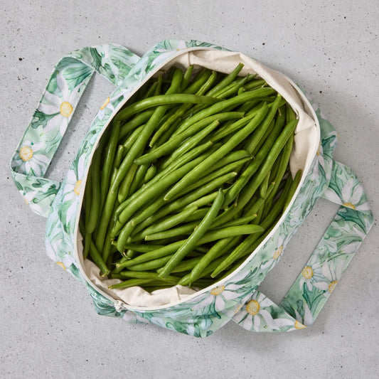 Green floral reusable produce bag filled with green beans on a grey surface