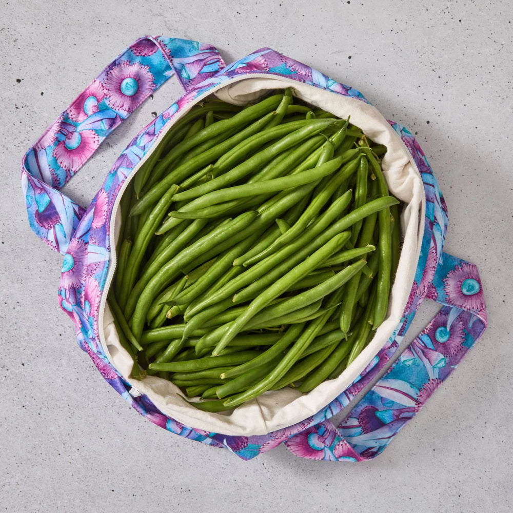 Purple floral reusable produce bag filled with green beans on a grey surface