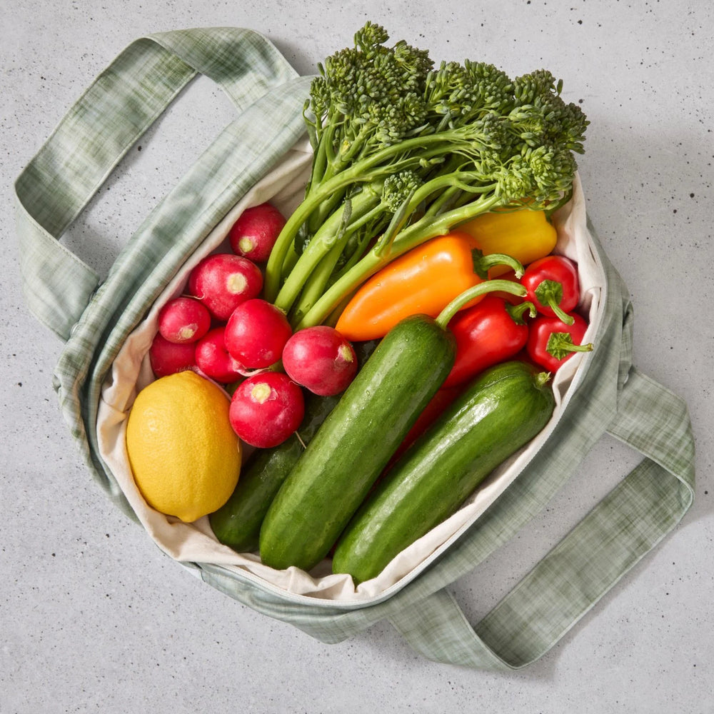 Green reusable produce bag filled with colourful vegetables on a grey surface