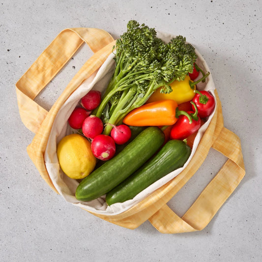 Yellow reusable produce bag filled with colourful vegetables on a grey surface