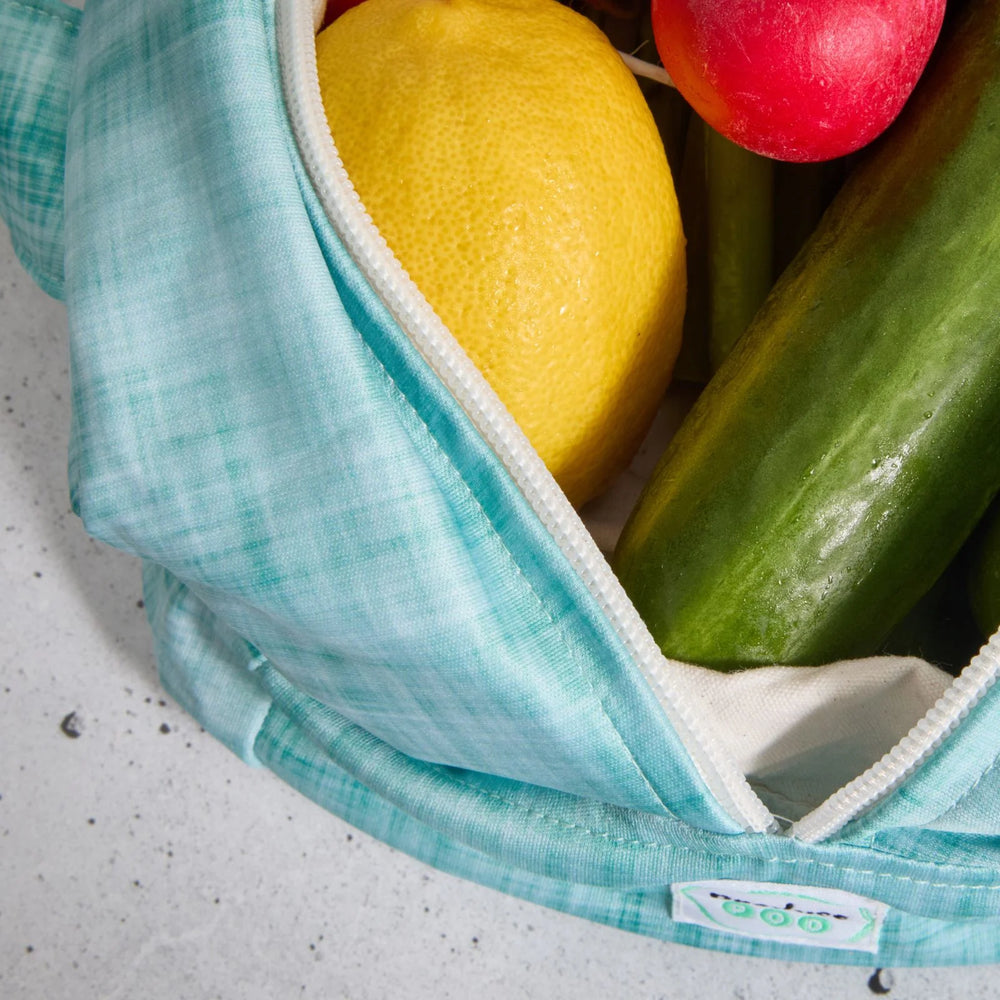 Teal reusable produce bag filled with fresh produce including radishes, a lemon, and cucumbers.