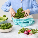 Person using a reusable produce bag with green vegetables in a kitchen