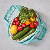 Teal reusable produce bag filled with colourful vegetables on a grey surface