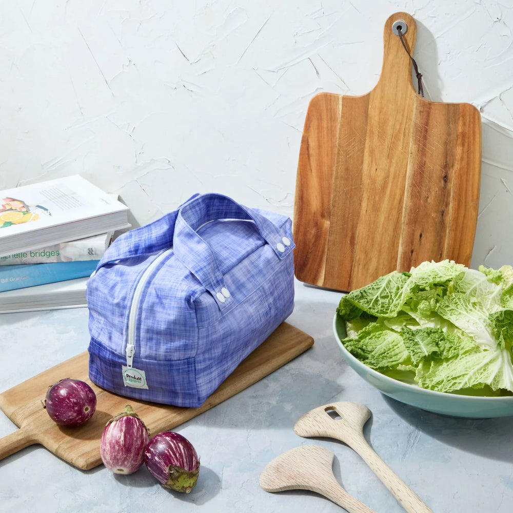 Purple reusable produce bag on a kitchen counter with a bowl of lettuce, cutting board, and baby eggplants.