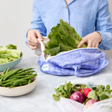 Person using a reusable produce bag with green vegetables in a kitchen