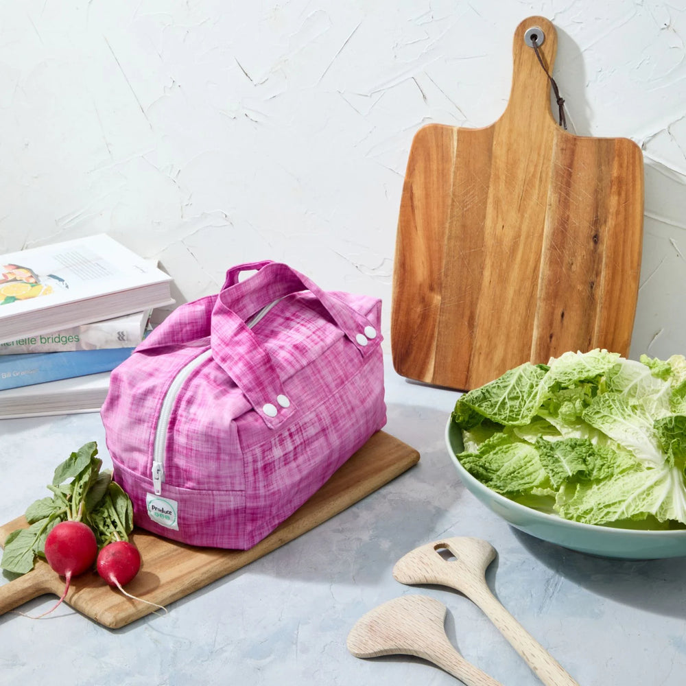 Pink reusable produce bag on a kitchen counter with a bowl of lettuce, cutting board, and radishes.