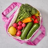 Pink reusable produce bag filled with colourful vegetables on a grey surface