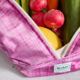 Pink reusable produce bag filled with fresh produce including radishes, a lemon, and cucumbers.
