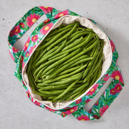Pink floral reusable produce bag filled with green beans on a grey surface