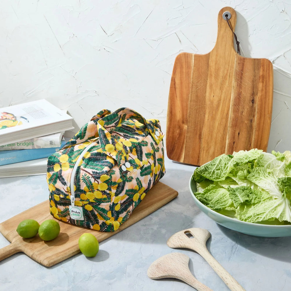 Yellow floral reusable produce bag on a kitchen counter with a bowl of lettuce, cutting board, and limes.