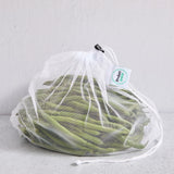 White drawstring mesh reusable produce bag filled with green beans on a light grey background