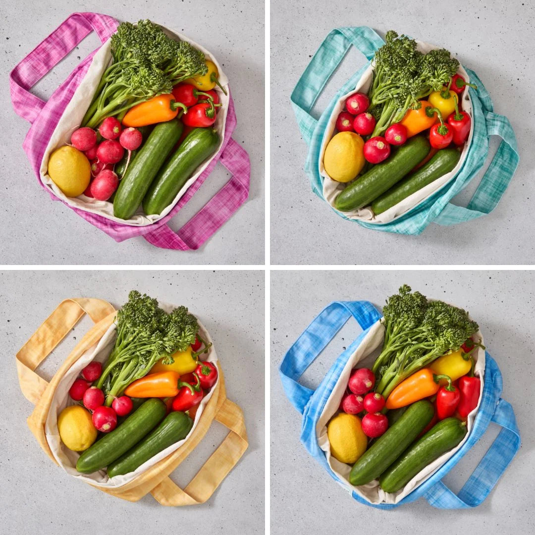 Four different colored reusable produce bags filled with fresh vegetables on a grey background.