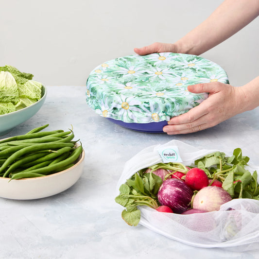 Person holding a floral-patterned reusable bowl cover over a bowl on a light surface.