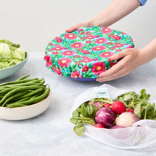 Person holding a floral-patterned reusable bowl cover over a bowl on a light surface.
