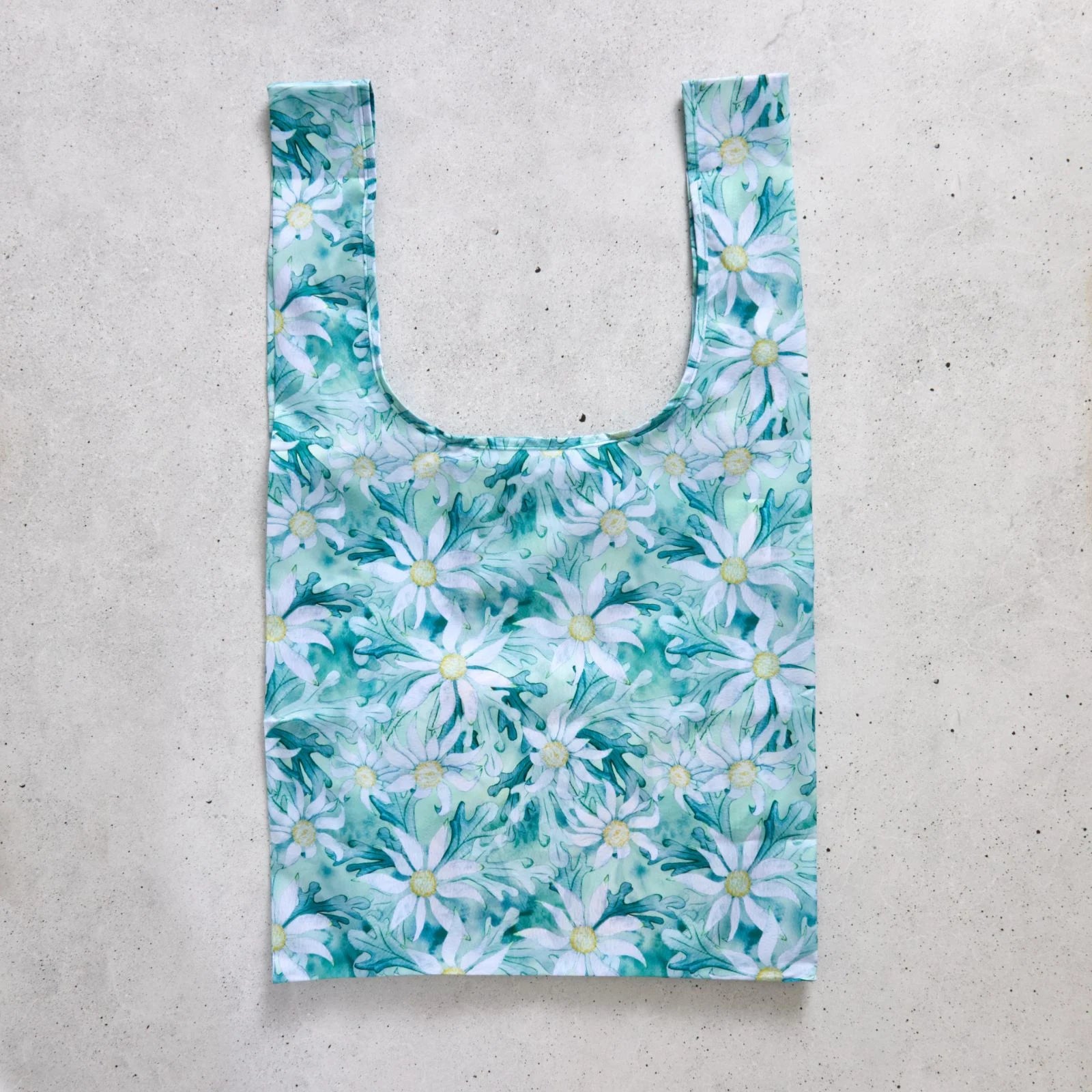 Reusable shopping bag with green floral pattern on a concrete surface