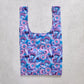 Reusable shopping bag with purple floral pattern on a concrete surface