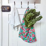 Green leafy vegetables in a reusable shopper bag hanging on a white door with hooks.