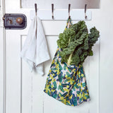 Green leafy vegetables in a reusable shopper bag hanging on a white door with hooks.