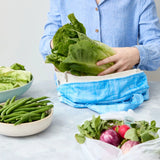 Person using a reusable produce bag with green vegetables in a kitchen