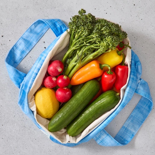 Blue reusable produce bag filled with colourful vegetables on a grey surface