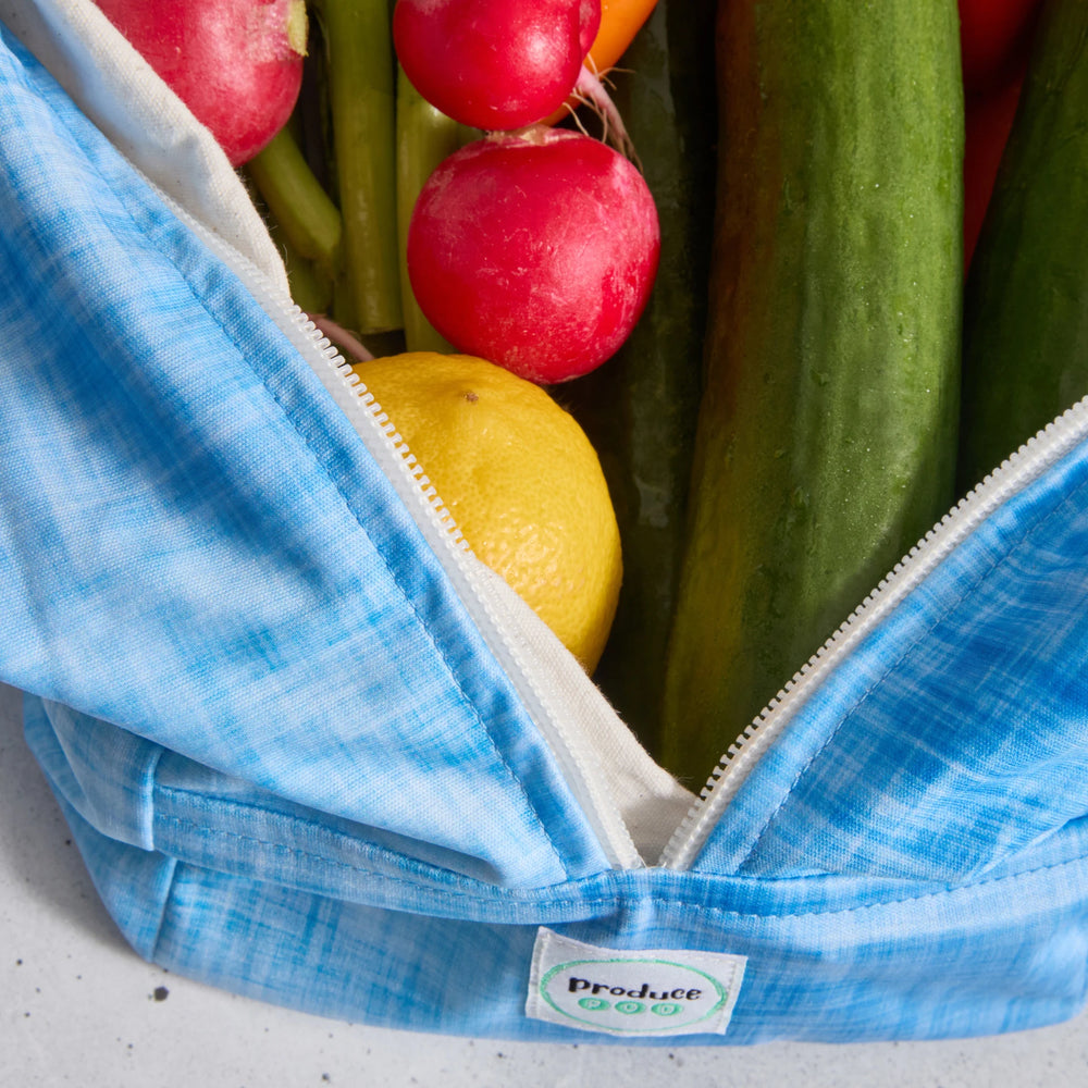 Blue reusable produce bag filled with fresh produce including radishes, a lemon, and cucumbers.