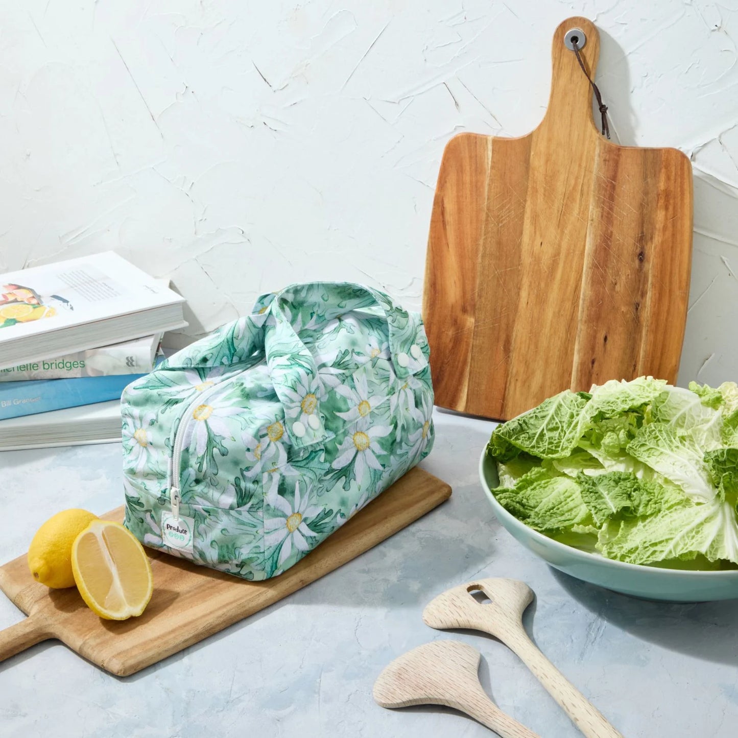 Green floral reusable produce bag on a kitchen counter with a bowl of lettuce, cutting board, and lemons.