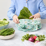 Person using a reusable produce bag with green vegetables in a kitchen