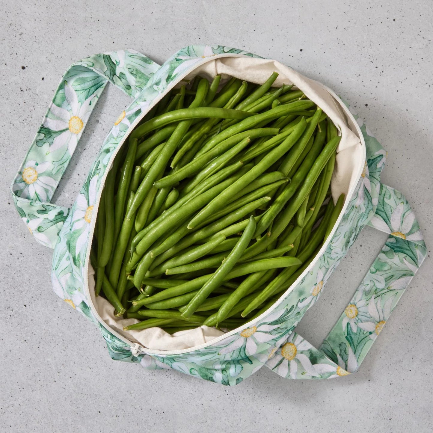 Green floral reusable produce bag filled with green beans on a grey surface