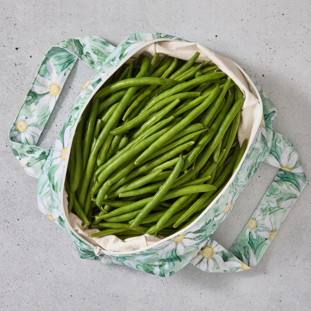 Green floral reusable produce bag filled with green beans on a grey surface