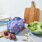 Purple floral reusable produce bag on a kitchen counter with a bowl of lettuce, cutting board, and baby eggplants