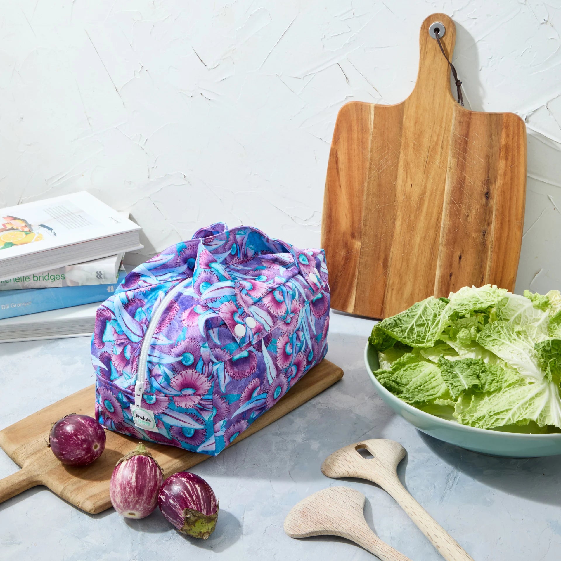 Purple floral reusable produce bag on a kitchen counter with a bowl of lettuce, cutting board, and baby eggplants