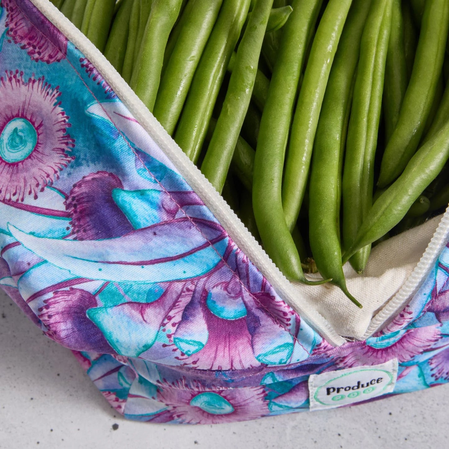Green beans in a reusable produce bag with floral pattern on a grey surface