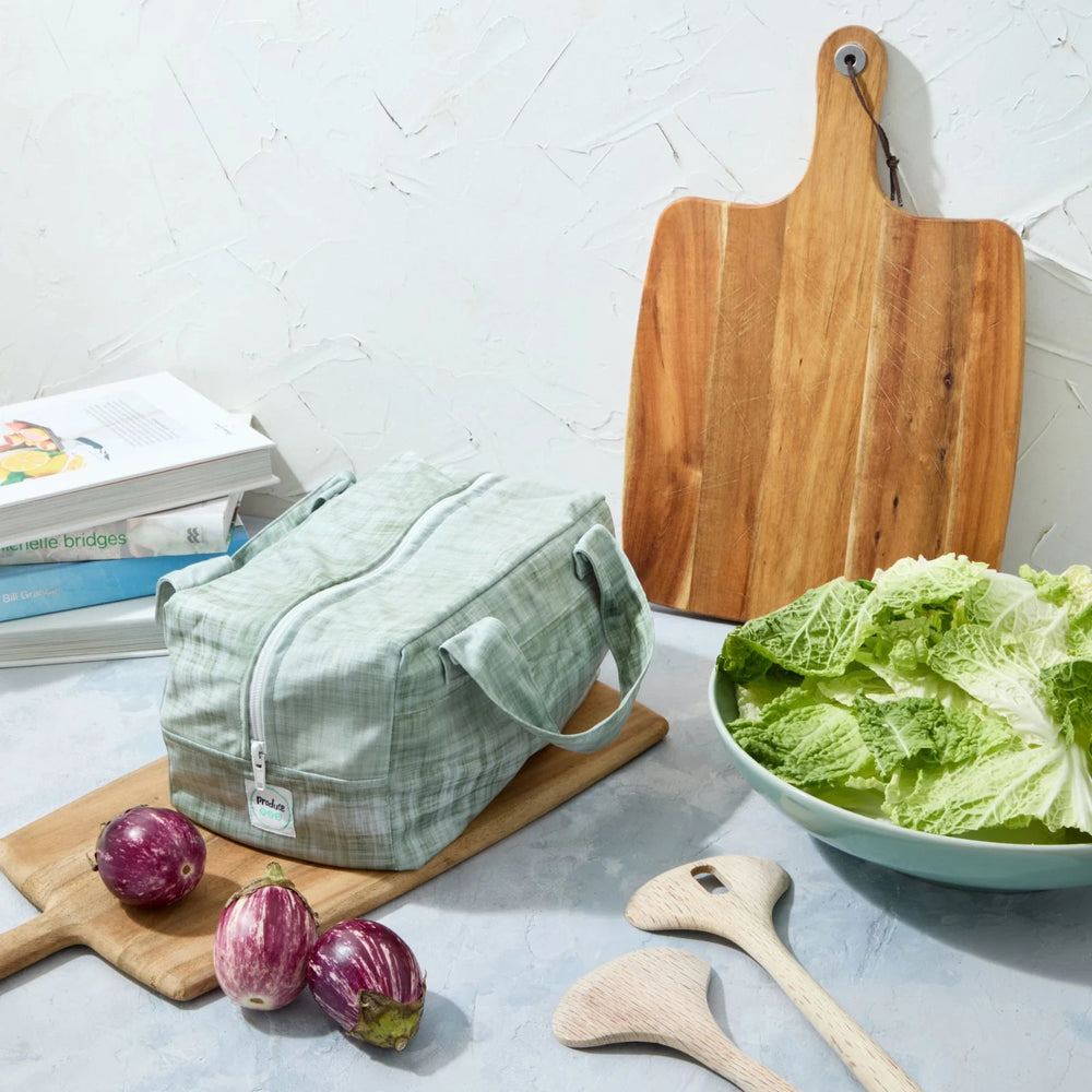 Green reusable produce bag on a kitchen counter with a bowl of lettuce, cutting board, and baby eggplants.