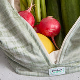 Green reusable produce bag filled with fresh produce including radishes, a lemon, and cucumbers.