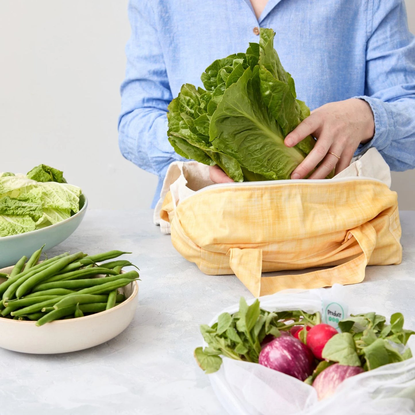 Person using a reusable produce bag with green vegetables in a kitchen
