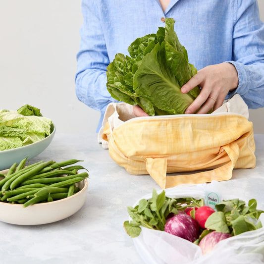 Person using a reusable produce bag with green vegetables in a kitchen