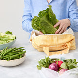 Person using a reusable produce bag with green vegetables in a kitchen