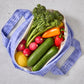 Purple reusable produce bag filled with colourful vegetables on a grey surface