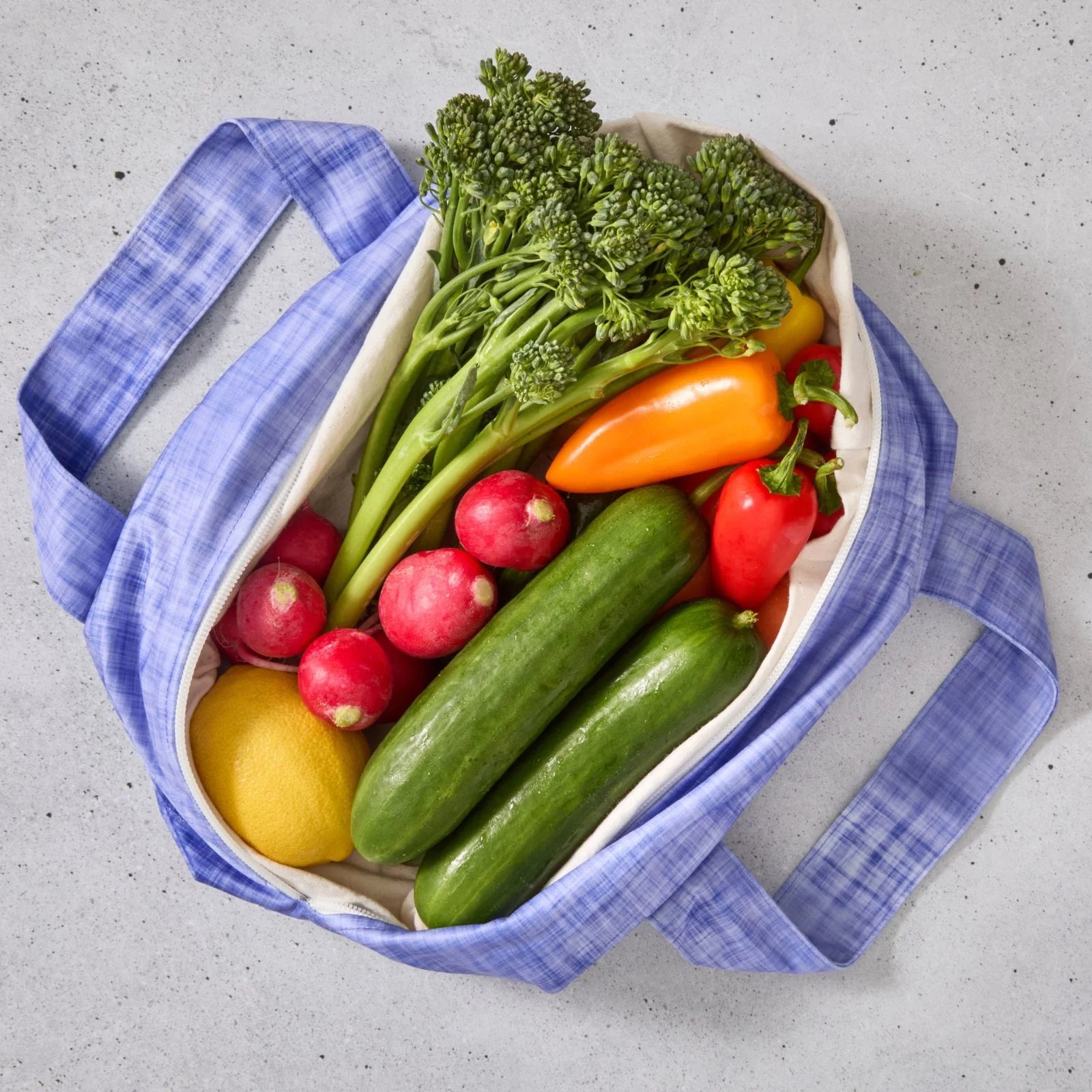 Purple reusable produce bag filled with colourful vegetables on a grey surface