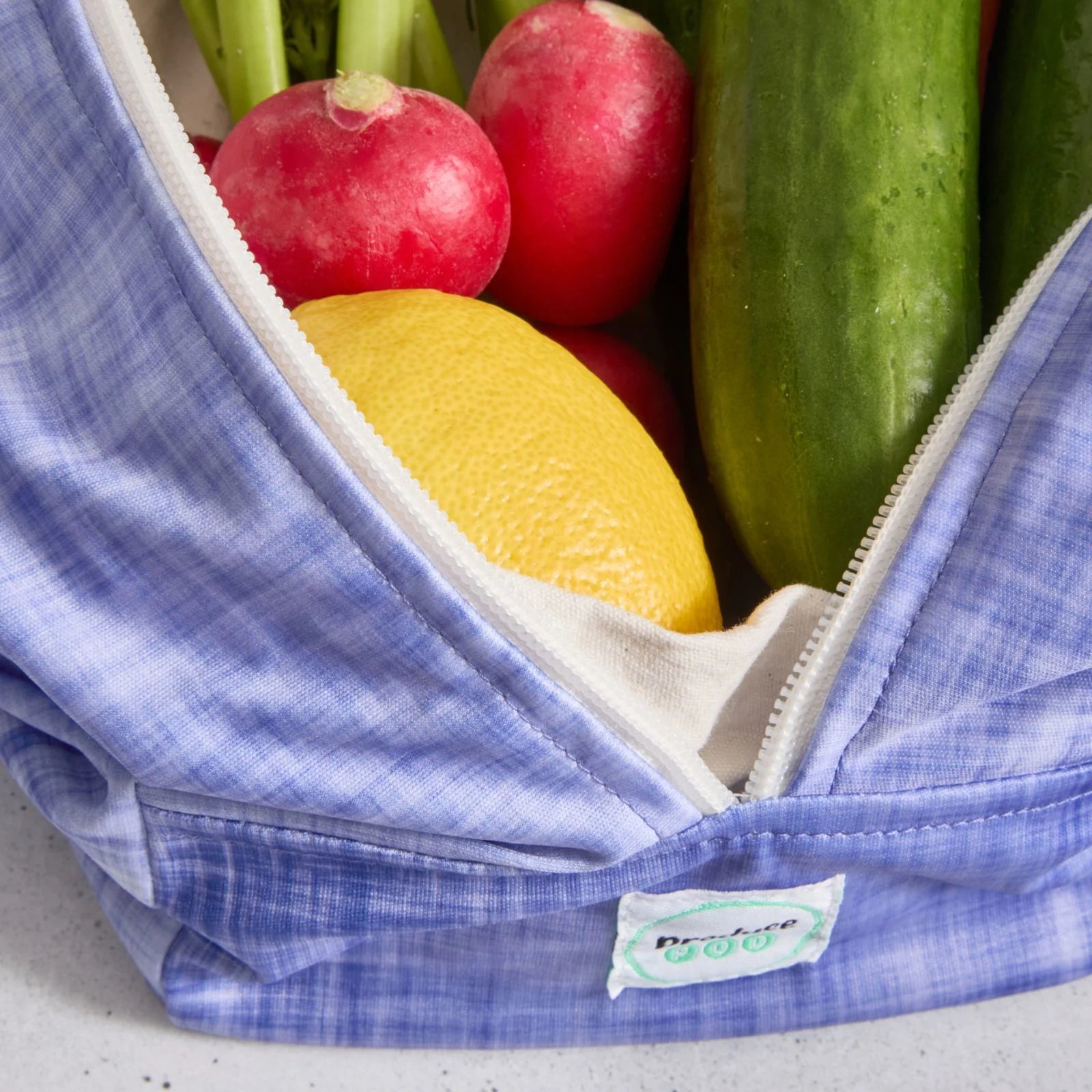 Purple reusable produce bag filled with fresh produce including radishes, a lemon, and cucumbers.