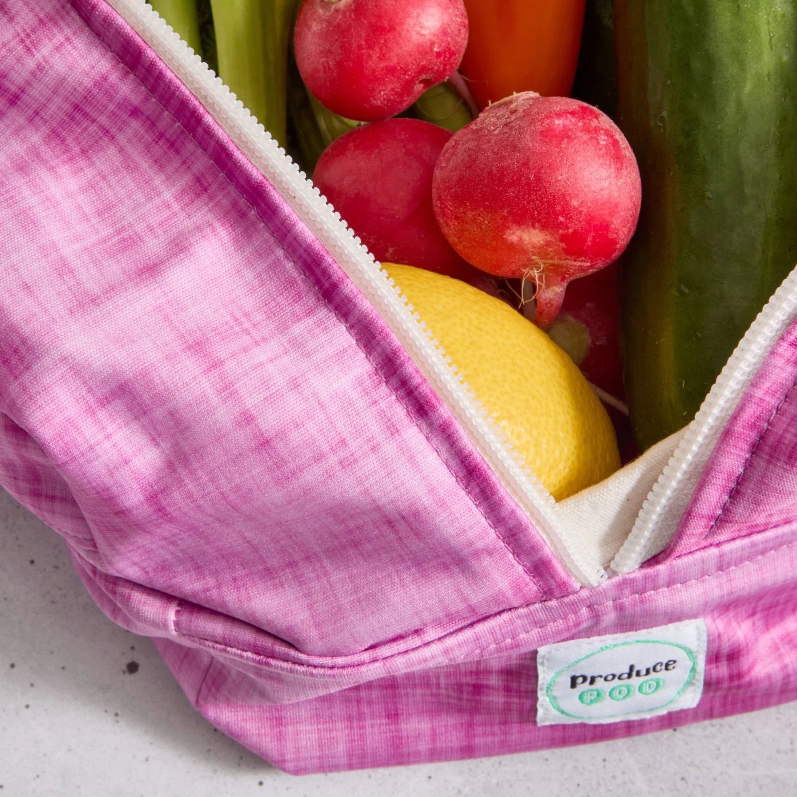 Pink reusable produce bag filled with fresh produce including radishes, a lemon, and cucumbers.