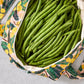 Green beans in a floral-patterned reusable produce bag on a grey surface