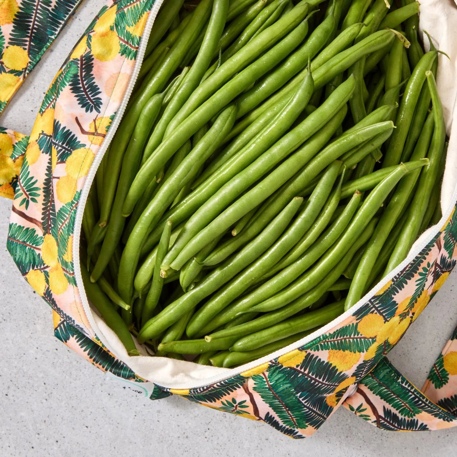 Green beans in a floral-patterned reusable produce bag on a grey surface