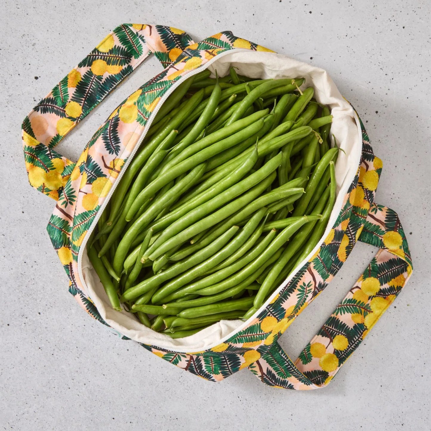 Yellow floral reusable produce bag filled with green beans on a grey surface